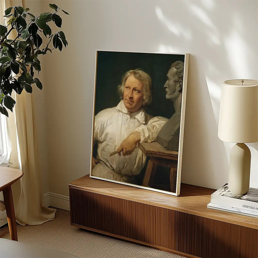Painting of a man with long hair and a white shirt, looking towards a bust, displayed on a wooden side table in a well-lit room with a lamp and plant.