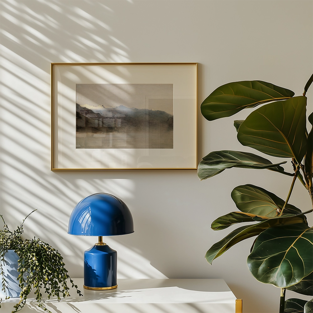 Framed painting of a serene landscape with mountains, displayed on a wall beside a blue lamp and a potted plant.
