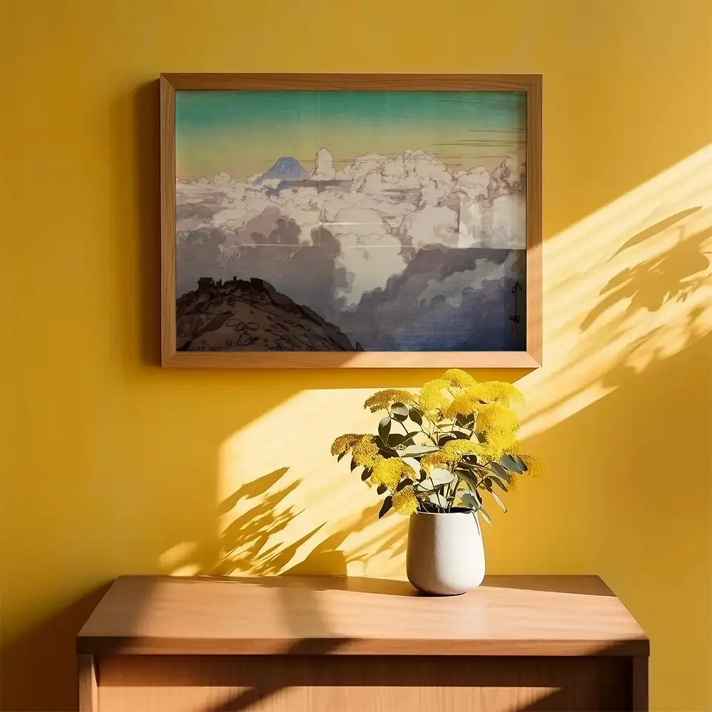 Framed painting of clouds and mountains on a yellow wall with a vase of yellow flowers on a wooden table