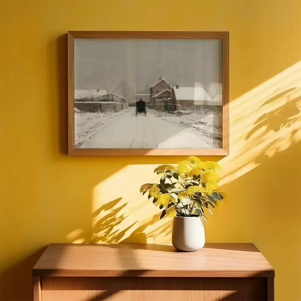 A framed painting of a snowy road leading to a house, displayed on a yellow wall above a wooden dresser with a vase of yellow flowers.