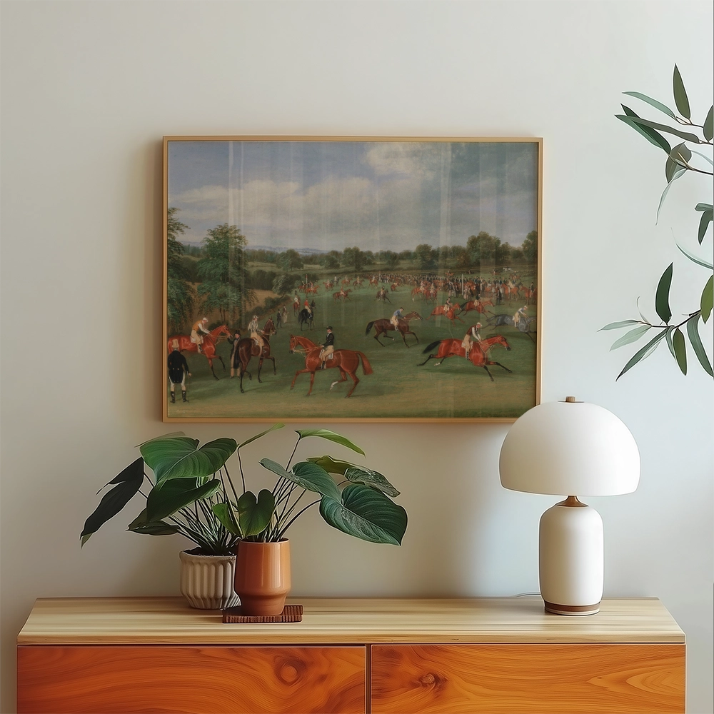 Painting of a lively horse racing scene framed on a wall above a wooden sideboard with a potted plant and a modern lamp.
