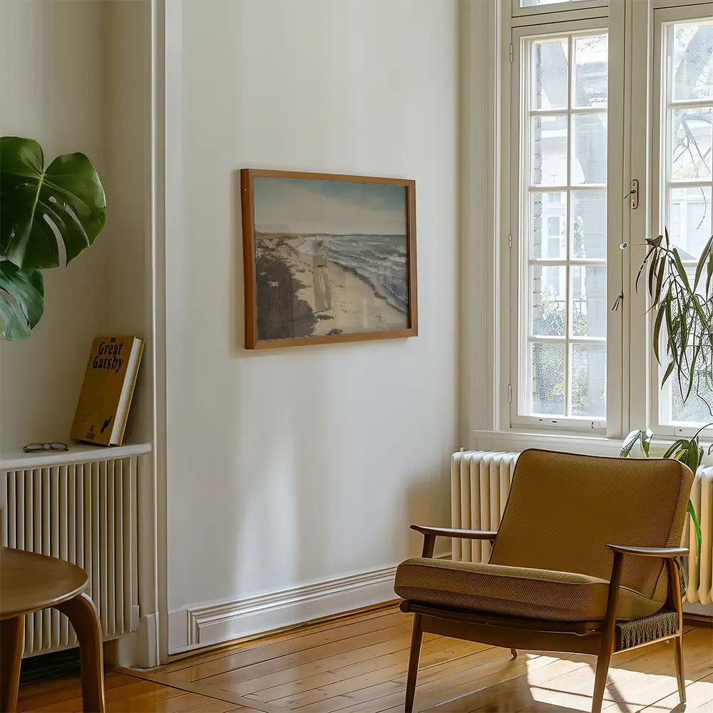 Painting of a coastal scene framed and hung on a wall in a modern interior with a brown chair and a houseplant.