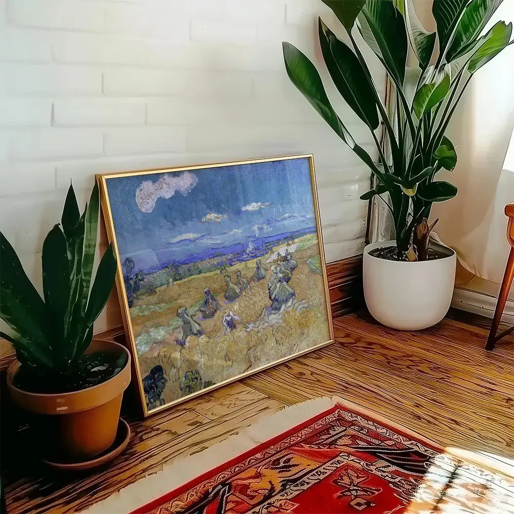 Framed painting of a rural landscape with people harvesting in golden fields, displayed in a cozy interior setting with plants and a patterned rug.
