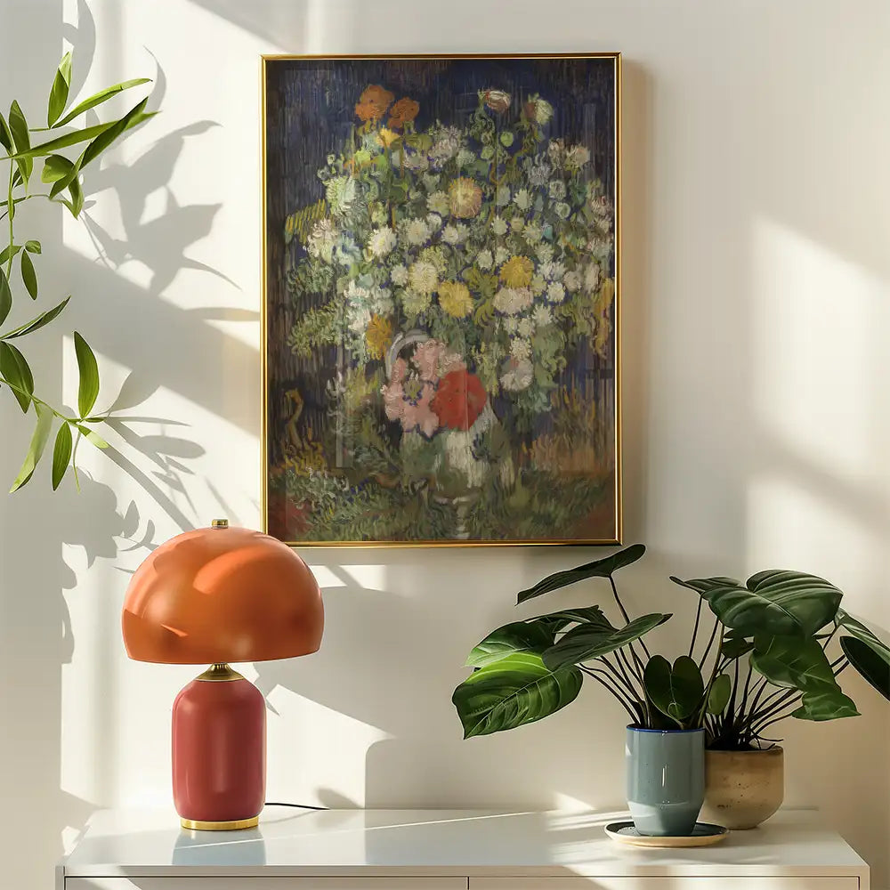 A colorful floral painting in a gold frame displayed on a wall, accompanied by a modern orange lamp and green potted plants.