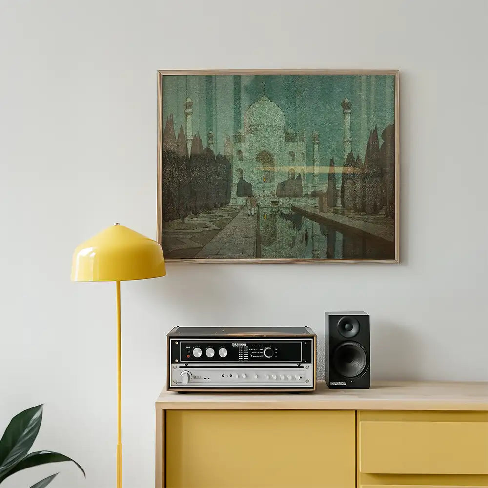 Framed painting of a serene landscape featuring a reflection pool and architectural elements, displayed above a yellow lamp and vintage audio equipment on a wooden cabinet.
