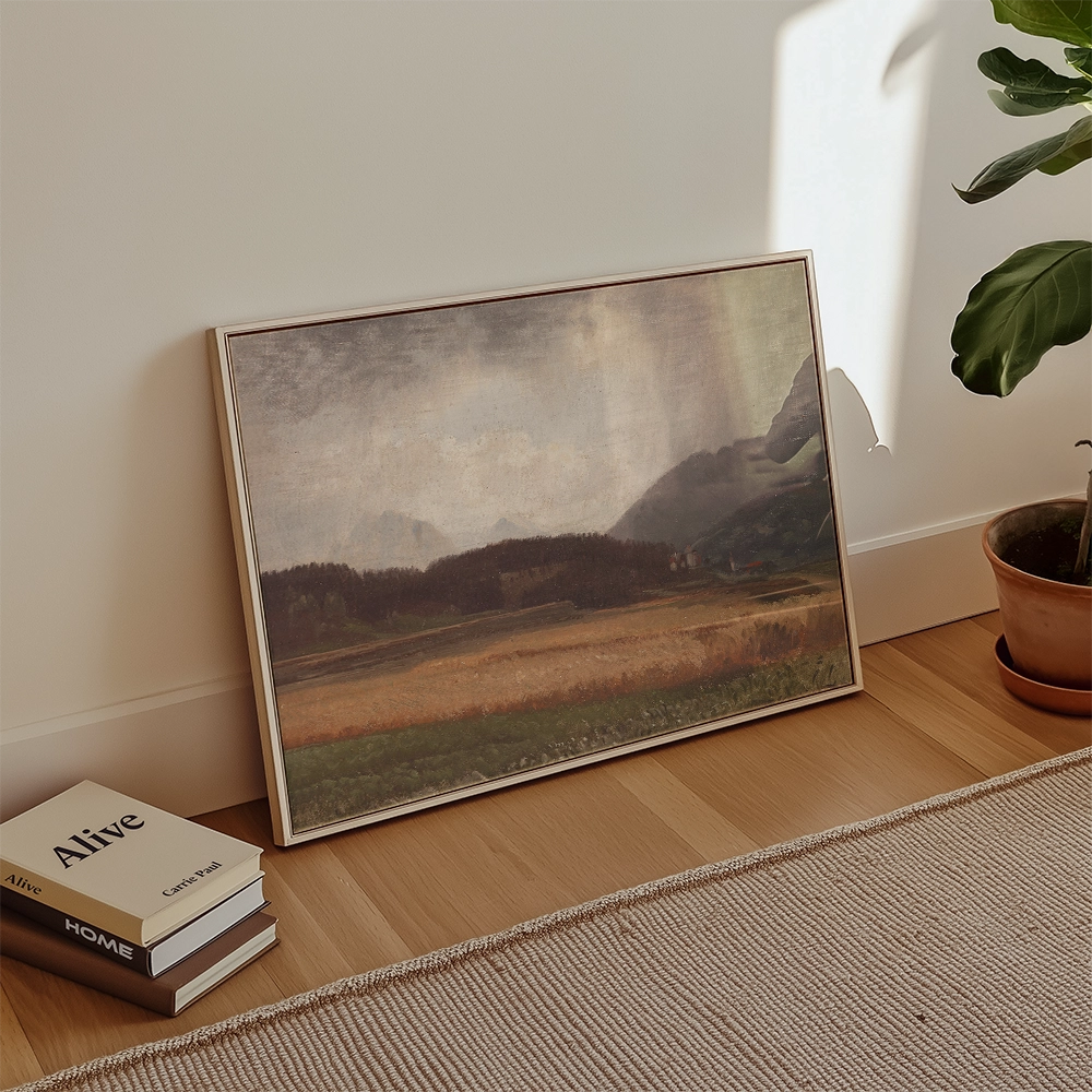 Framed painting of a serene landscape resting against a wall, with a small potted plant and decorative books nearby.