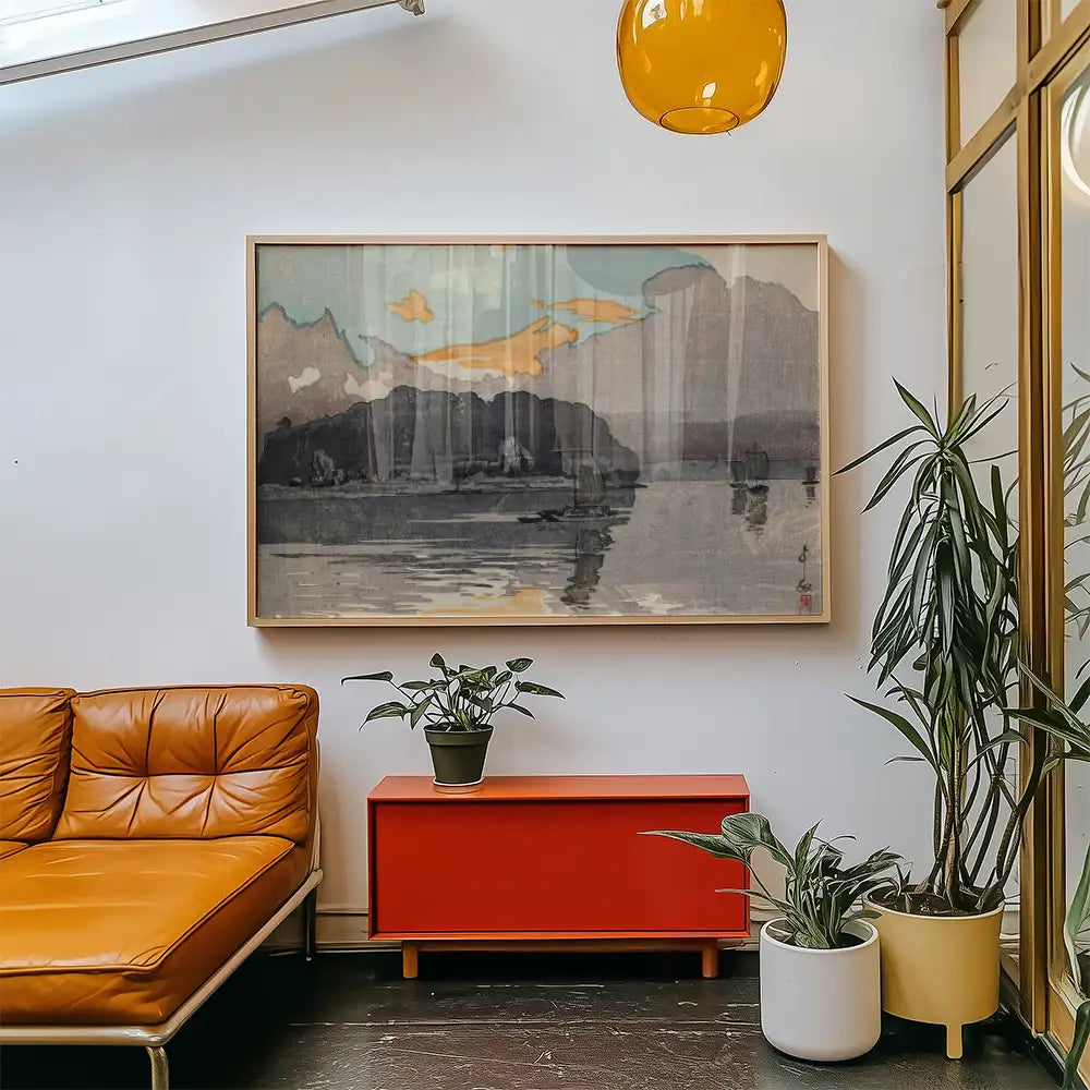 Modern art painting featuring a serene landscape with mountains and water, framed and displayed in a bright living space with a brown leather sofa and colorful plants.