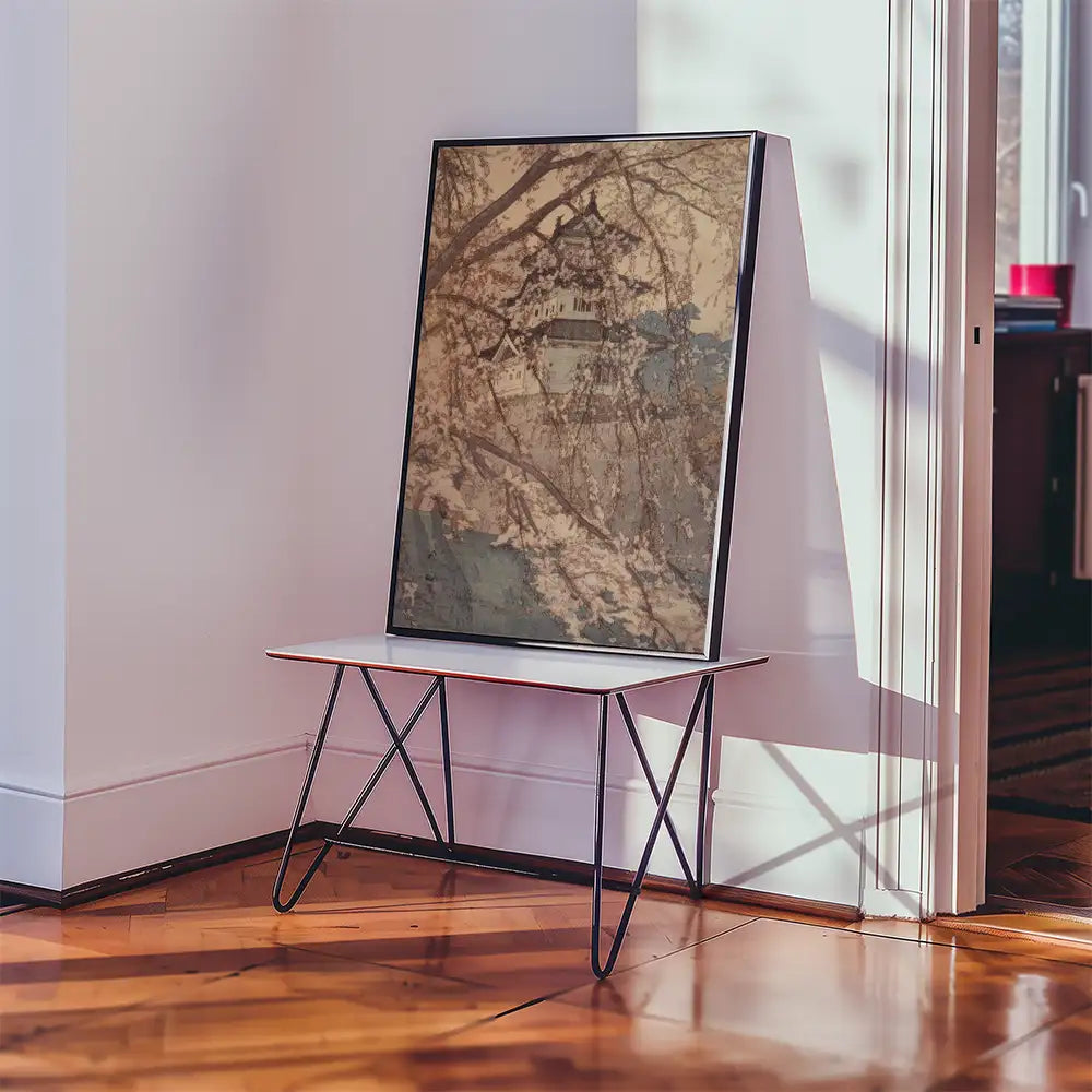 Framed artwork featuring a landscape scene displayed on a minimalist white table in a well-lit room.