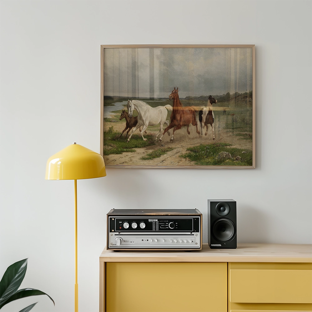 Painting of horses running along a river, framed and displayed above a modern yellow lamp and audio equipment on a wooden sideboard.