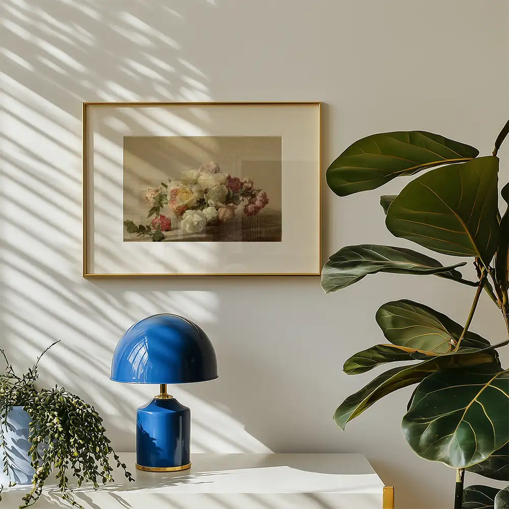 Framed vintage floral painting hanging on a wall above a blue lamp and greenery.
