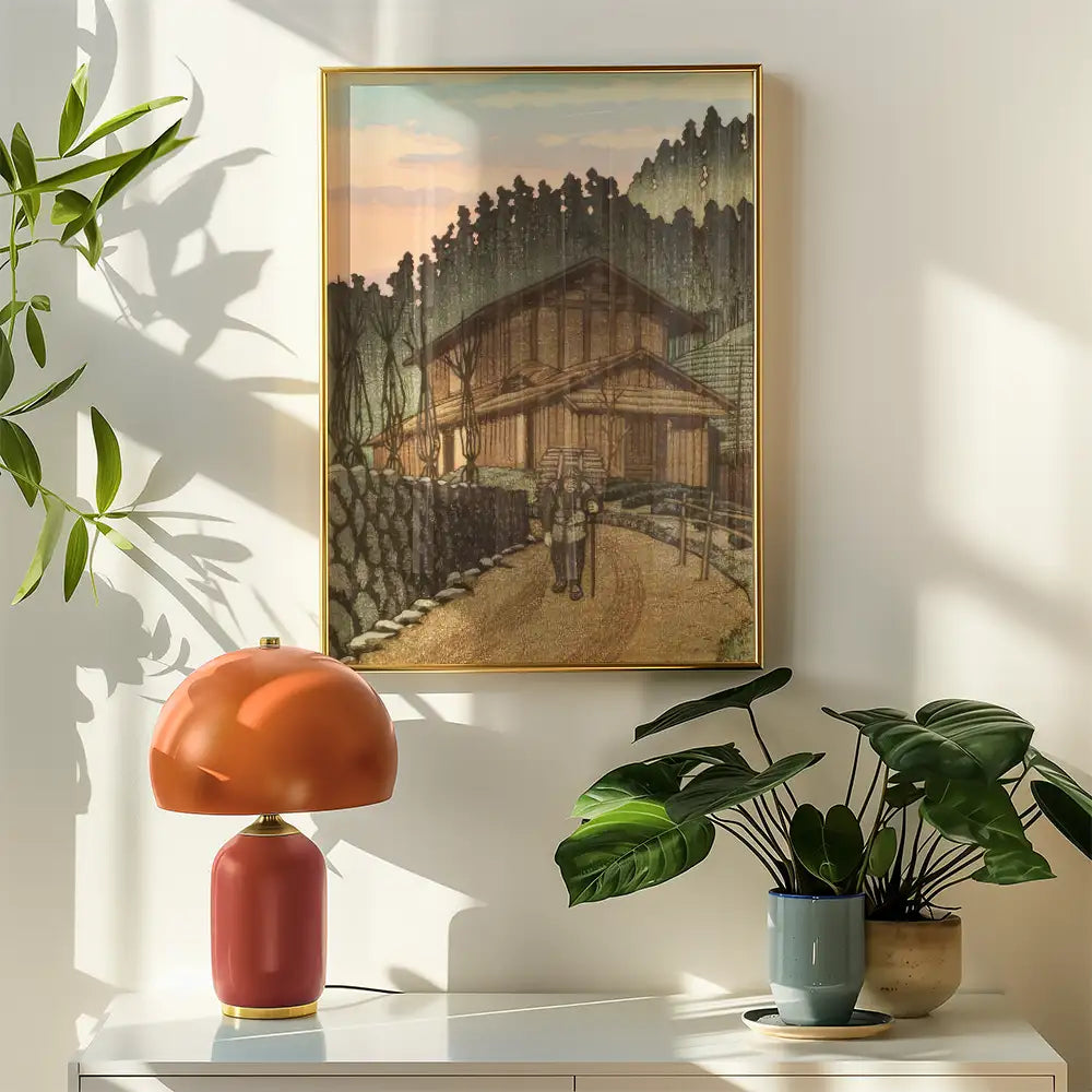 Rustic landscape painting of a hiker on a path with a house and trees in the background, framed and displayed on a wall next to a stylish lamp and potted plants.
