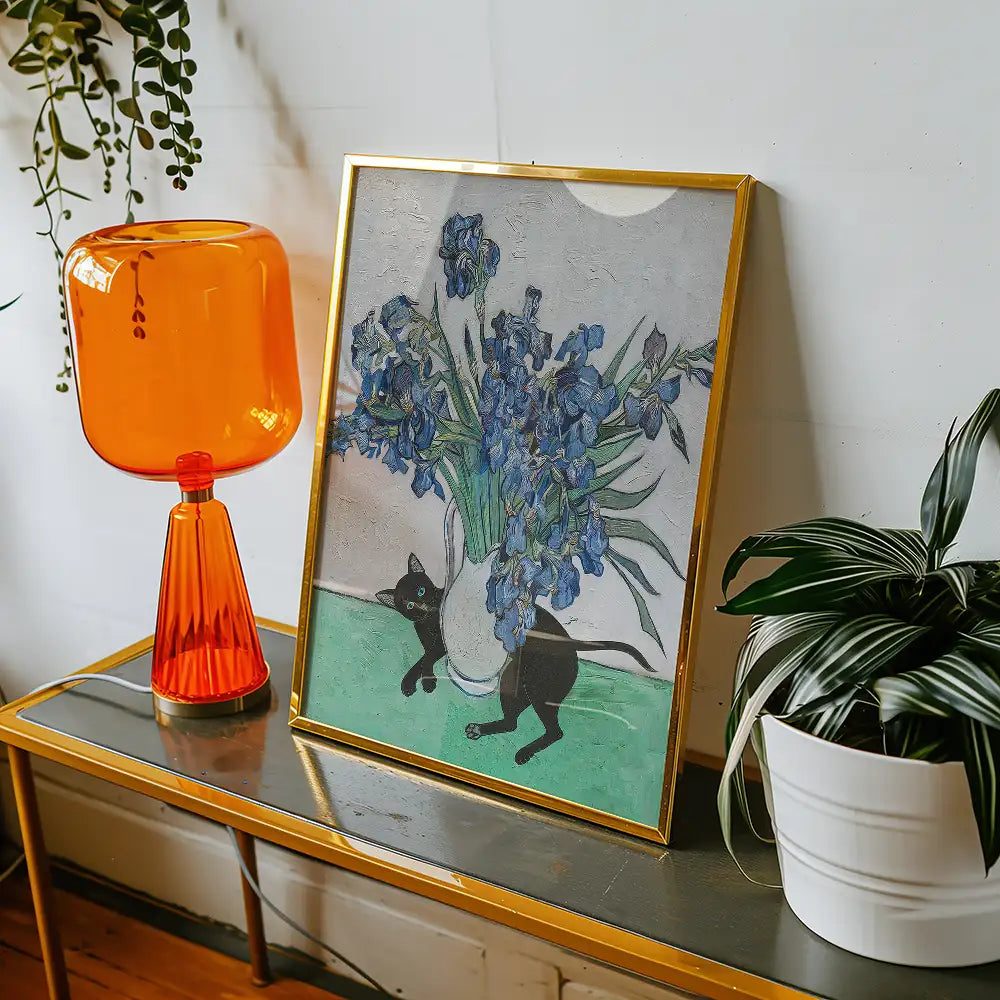 Painting of a black cat playing near a vase of blue irises, displayed in a gold frame with an orange lamp and green plant in the background.