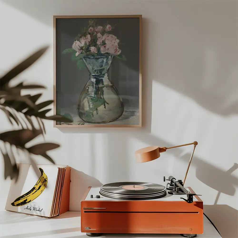 A framed painting of a flower vase with pink roses hanging on a wall above a retro record player and a banana artwork in a cozy interior setting.