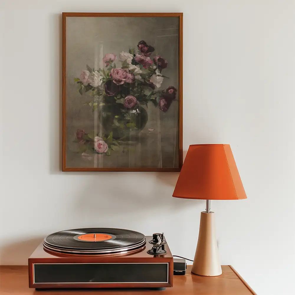 Floral painting in a wooden frame above a vintage record player and orange lampshade in a cozy interior setting.