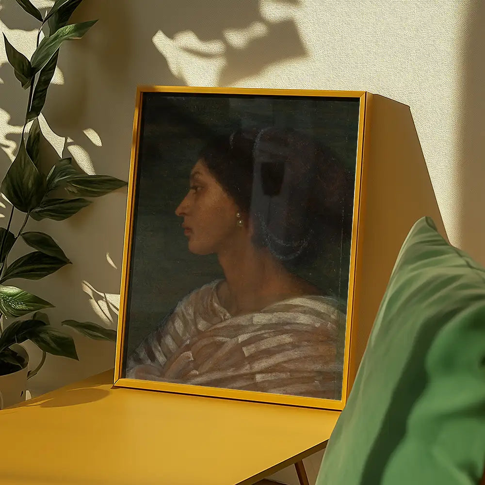 Framed portrait of a woman in profile, displayed on a yellow table with greenery in the background.