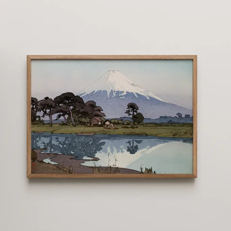 Framed painting of a mountain landscape reflecting in a calm body of water, featuring trees and a small hut in the foreground.