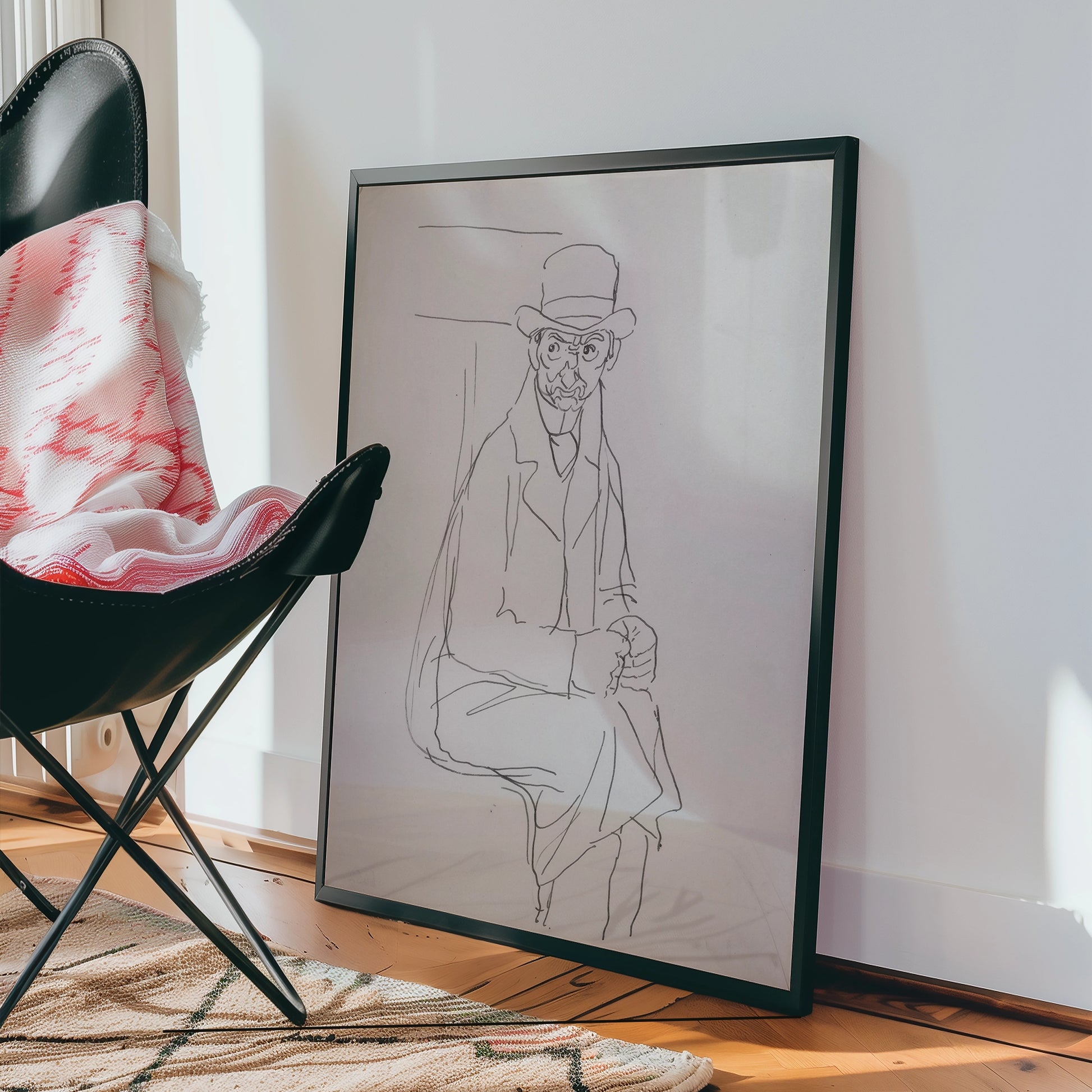 Framed line drawing of a seated man wearing a bowler hat, leaning against a wall, displayed next to a plush black chair and colorful blanket.