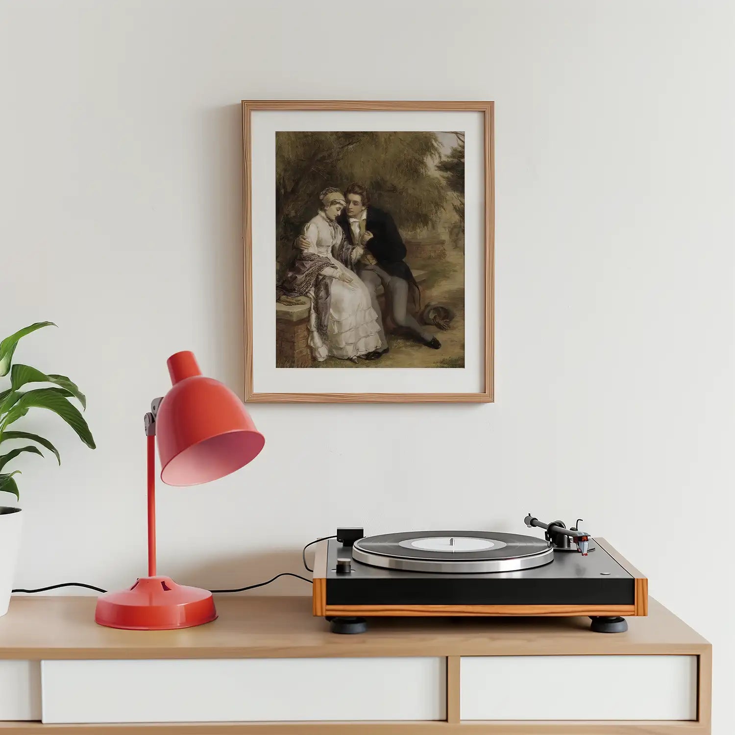 Framed painting of a couple in a romantic setting above a record player and a pink lamp on a wooden table, with a green plant in the background.