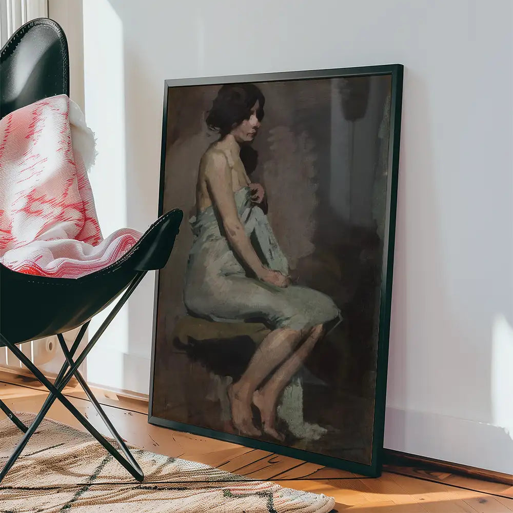 A framed painting of a seated woman draped in a light fabric, leaning against a neutral-colored background, placed next to a black chair and a patterned blanket on a wooden floor.