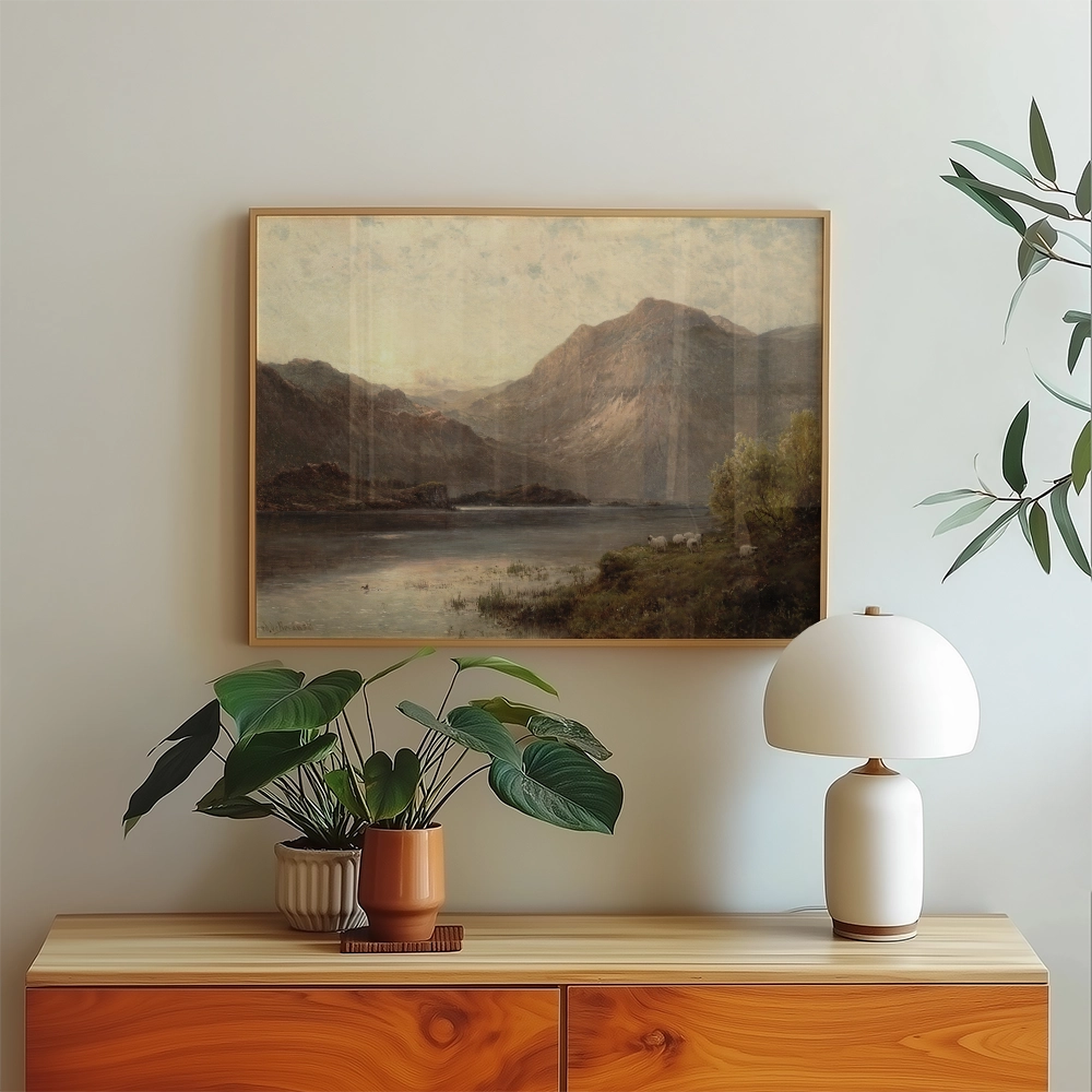 Framed landscape painting of mountains and a lake displayed above a wooden sideboard with a potted plant and a modern lamp.