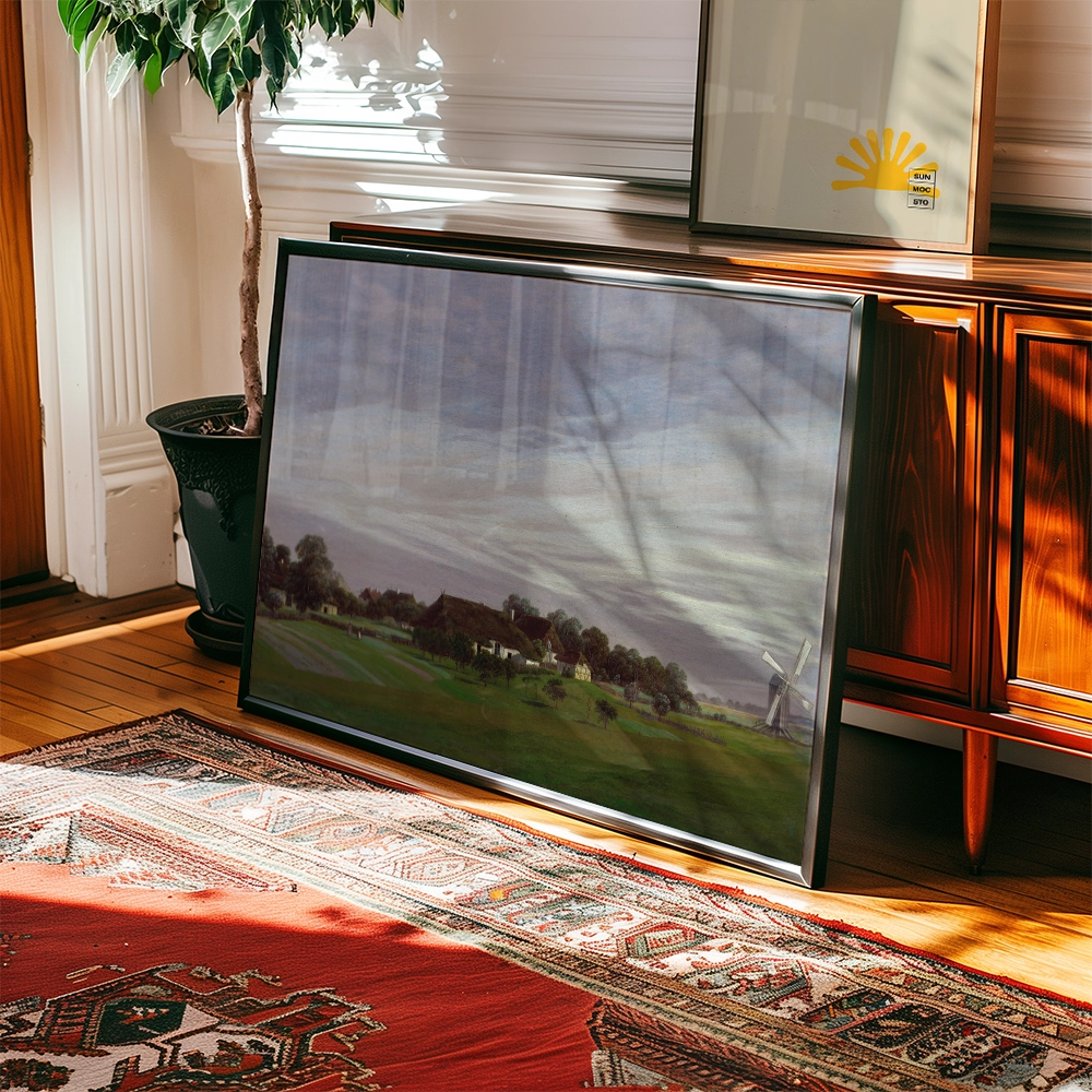 Framed landscape painting featuring a rural scene with a windmill, displayed on a wooden surface next to a plant.