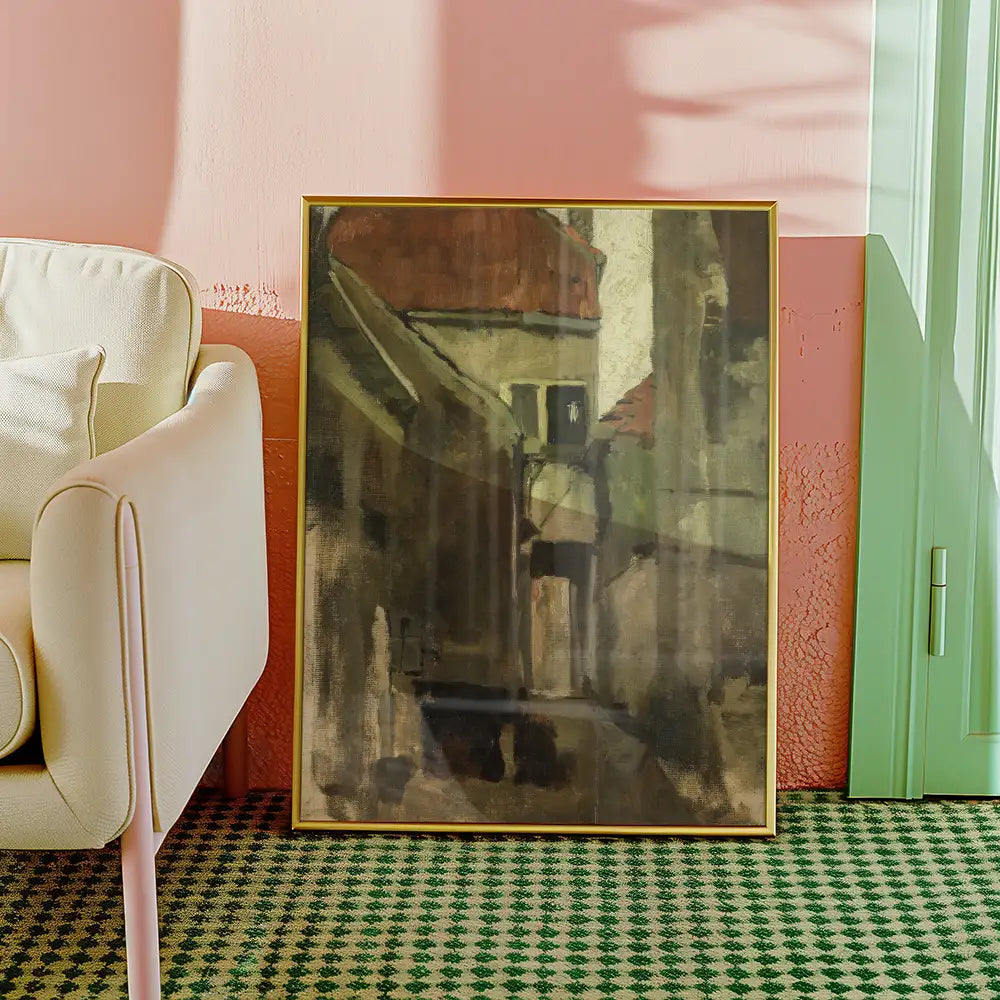 Abstract painting of a narrow street framed in gold, displayed beside a modern light-colored armchair in a stylish interior.