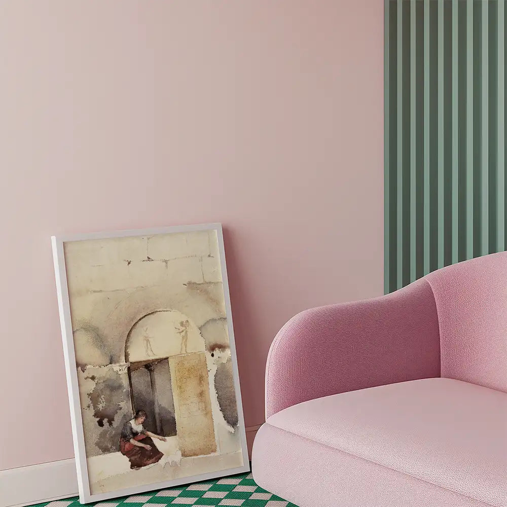 Framed watercolor painting of a woman near an archway, leaning against a stone wall, placed beside a pink sofa in a modern interior setting.