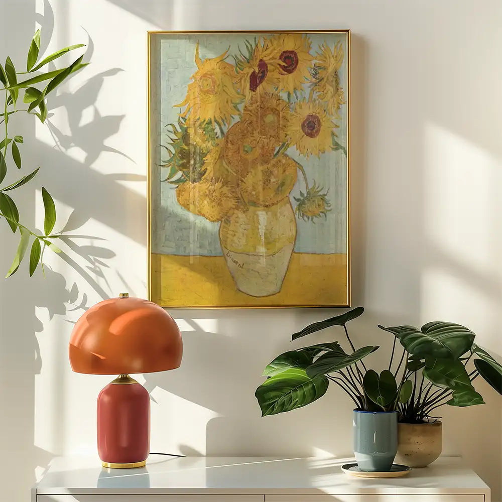 Framed painting of sunflowers in a vase hanging on a wall, accompanied by a modern lamp and potted plants on a white surface.