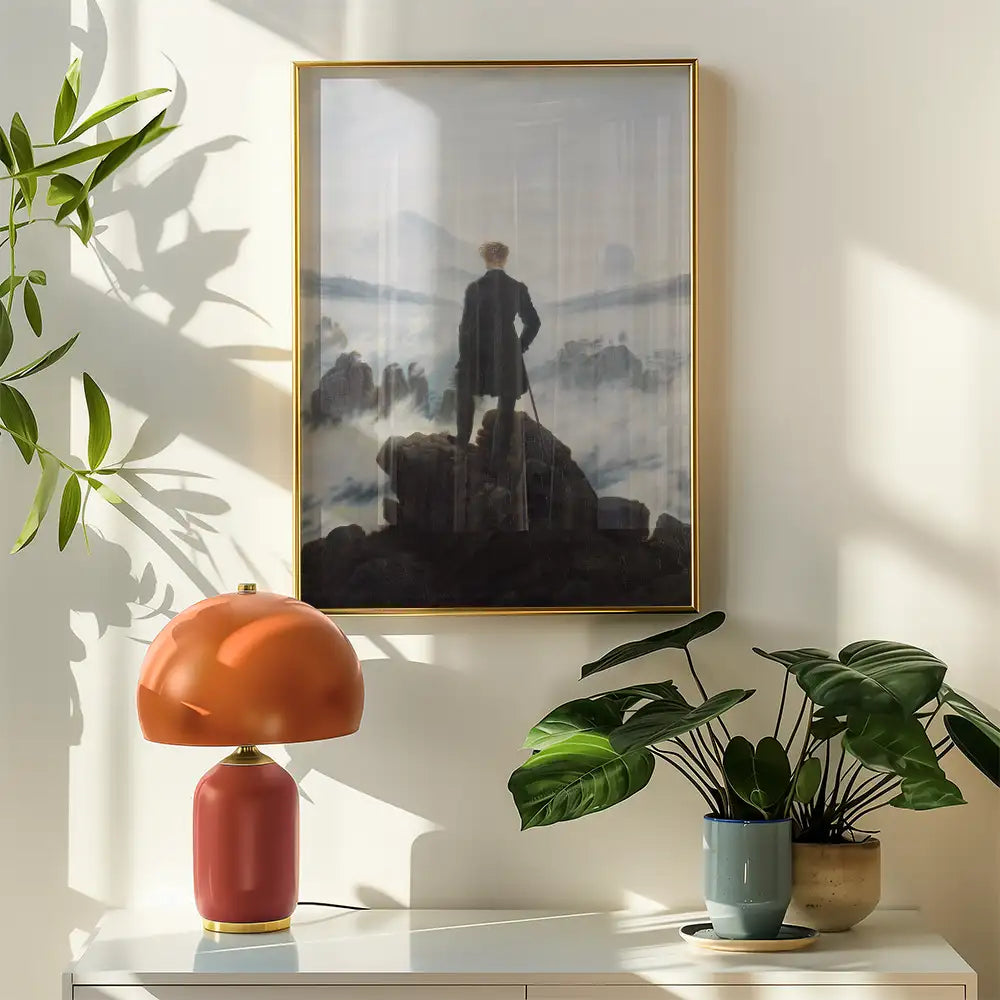 Framed painting of a figure standing atop a rock, gazing into a misty landscape, accompanied by a coral lamp and potted plants against a light wall.