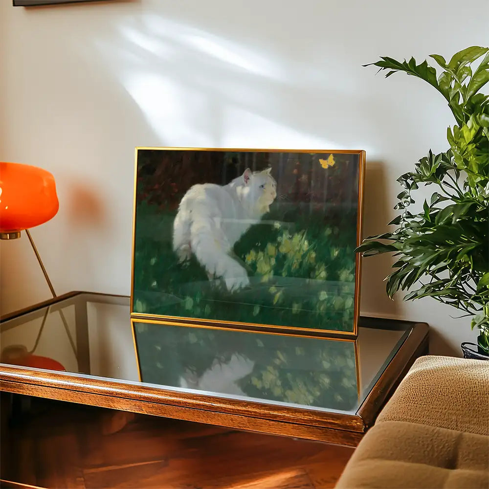 Painting of a white cat in a green garden with yellow flowers and a butterfly, displayed on a wooden table with a modern lamp beside it.
