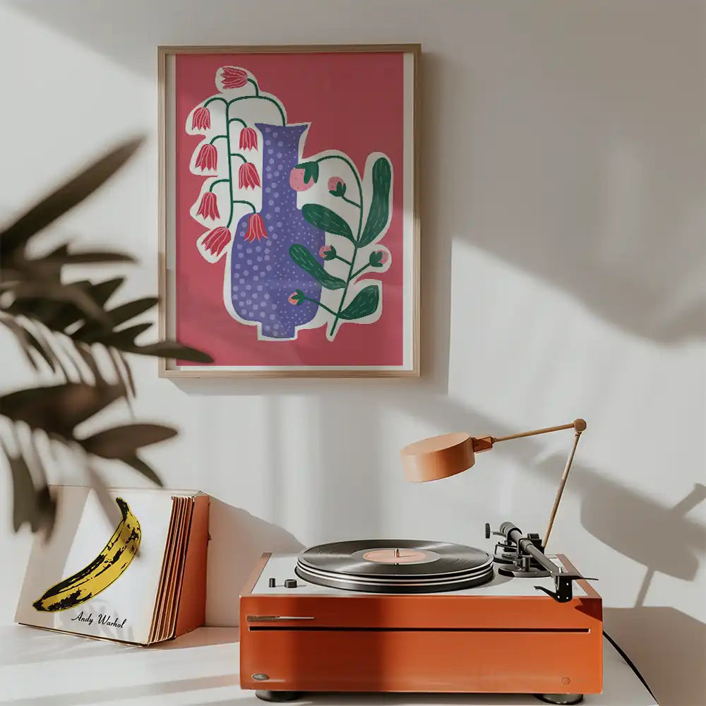 Modern art print featuring a stylized vase with flowers on a vibrant pink background, framed and displayed above a vintage record player in a contemporary setting.