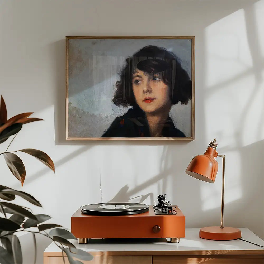Portrait painting of a young woman with dark hair in a gold frame, displayed above a vintage turntable and an orange desk lamp in a modern interior setting.