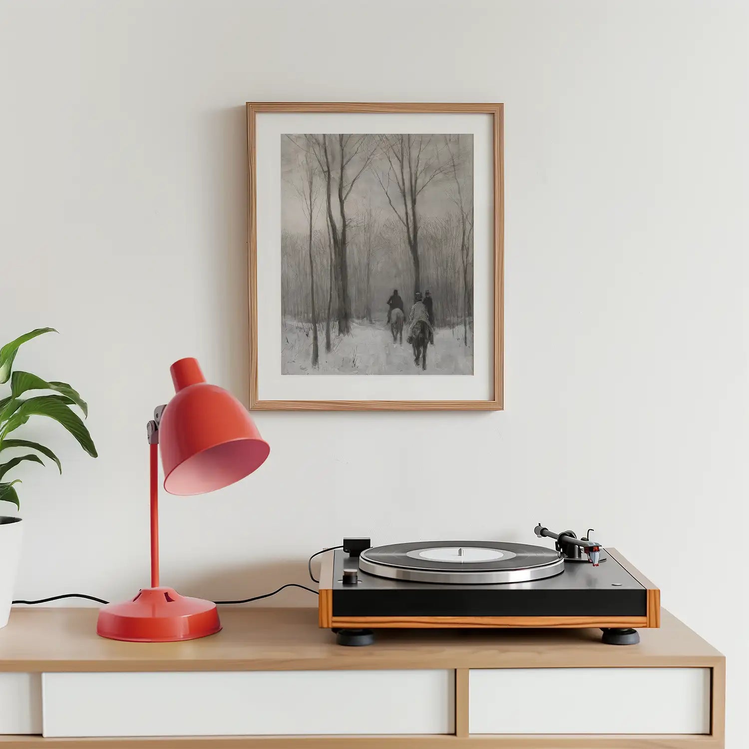 A framed painting of two horse riders in a snowy landscape, displayed above a record player and a red lamp on a wooden surface.