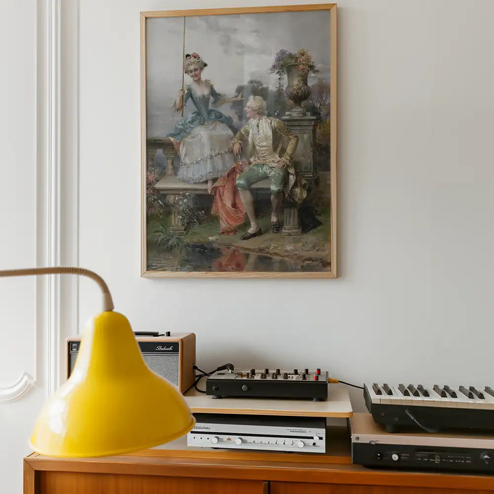 Framed vintage painting of a couple in historical clothing, sitting by a fountain, displayed on a white wall above a wooden cabinet with a yellow lamp and vintage audio equipment.