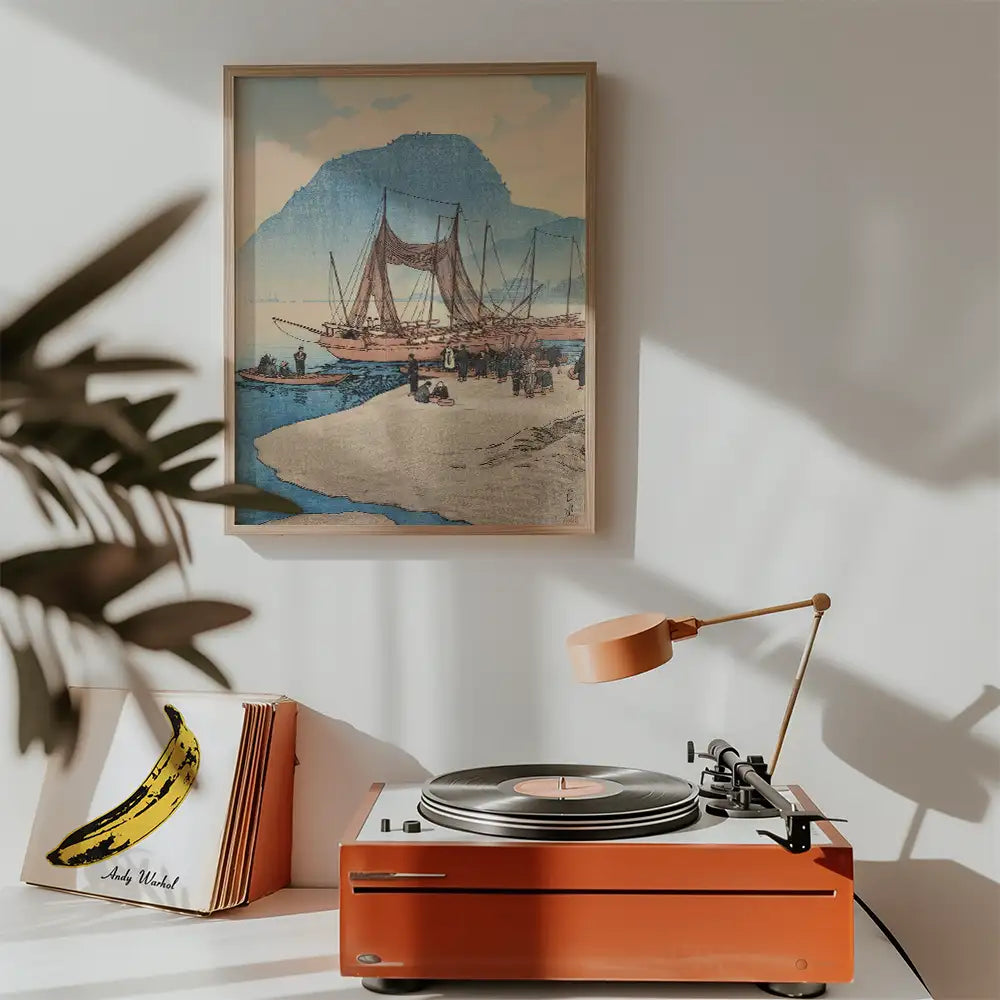 Painting of boats by a sandy shore with a mountain backdrop, framed and displayed above a modern record player and a banana-themed album cover.