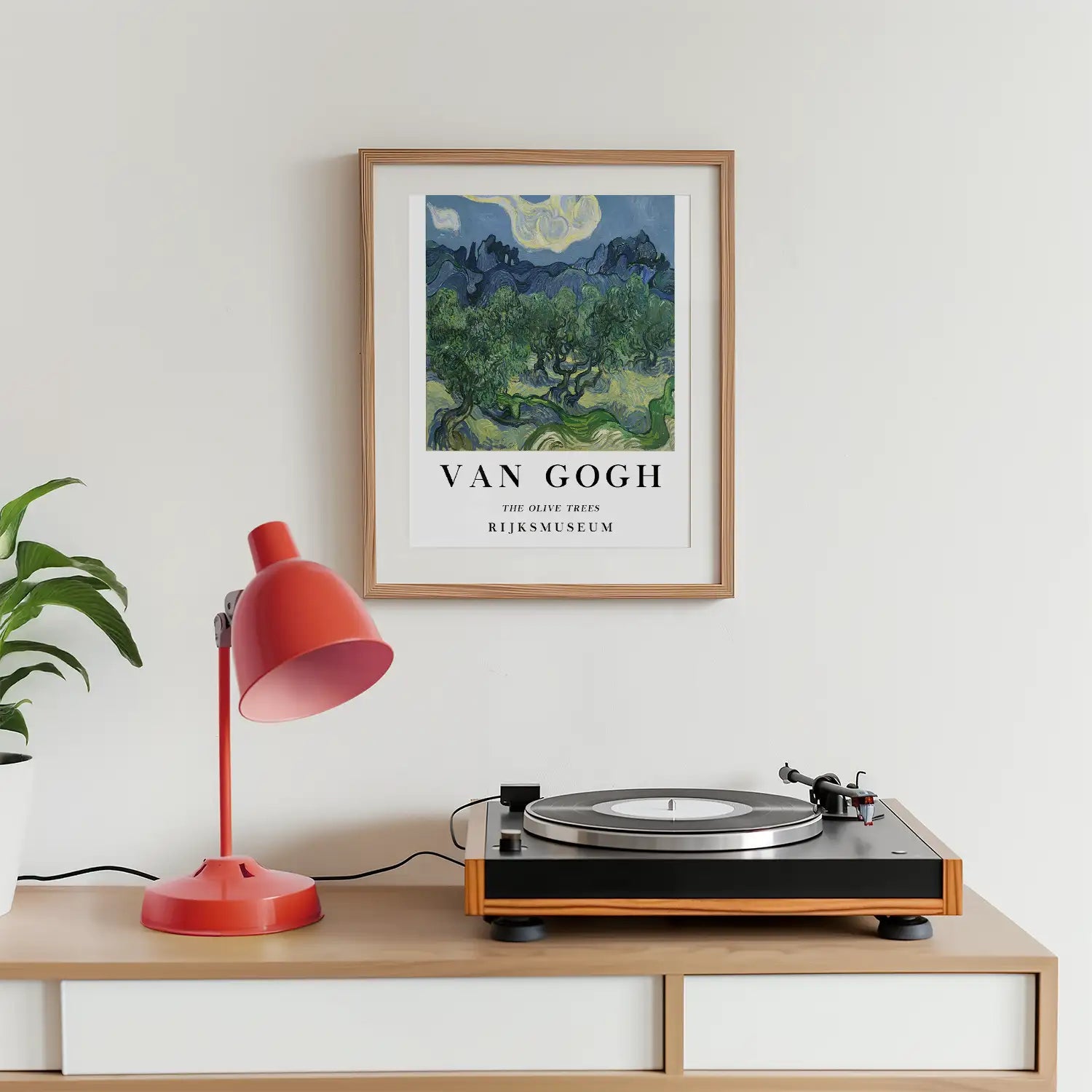 Framed painting of Van Gogh's "The Olive Trees" above a turntable and red lamp on a wooden surface.