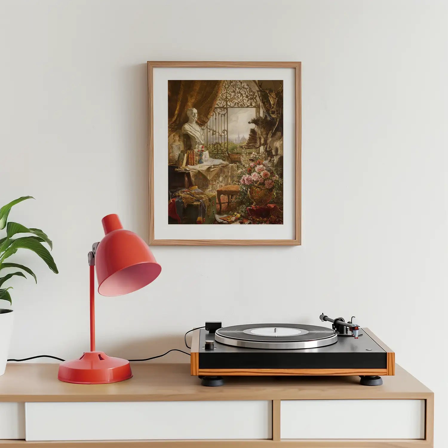 Framed painting featuring a classical interior scene with a statue, flowers, and a scenic view, positioned above a turntable and red lamp on a wooden surface.