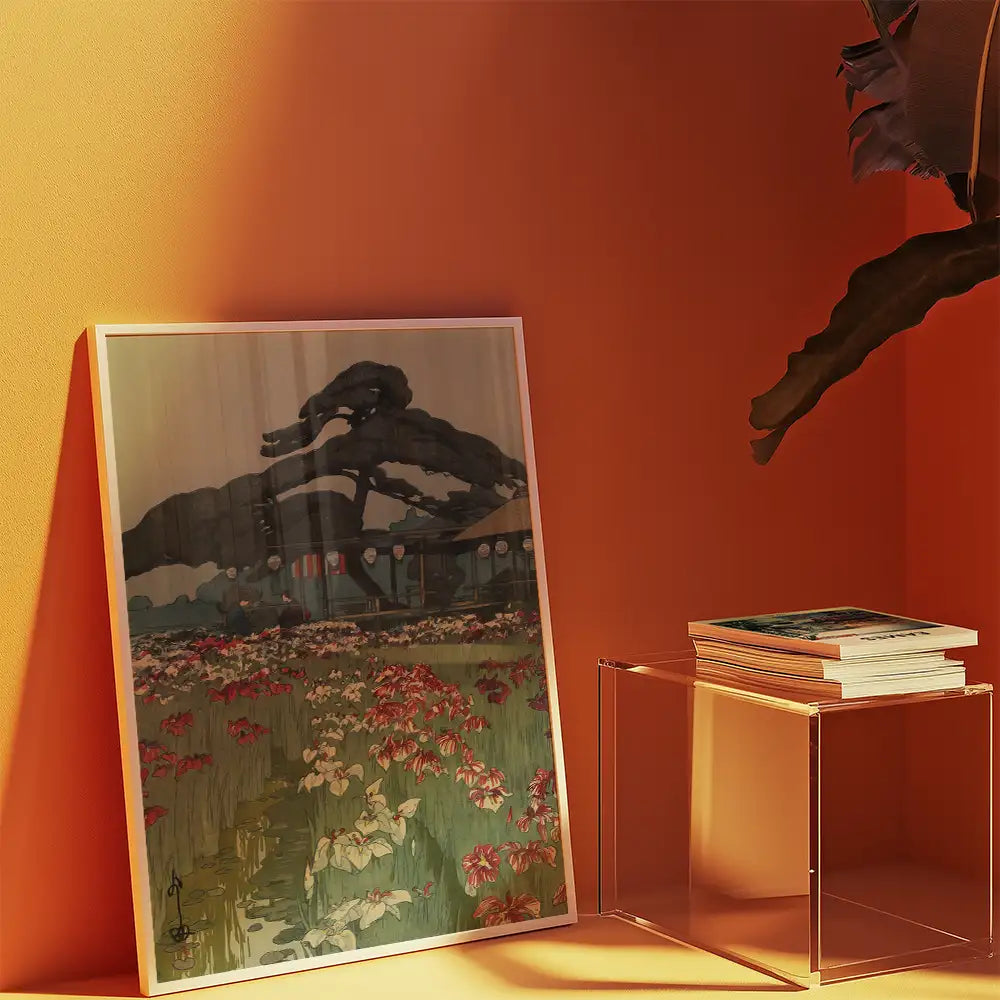 Artistic painting featuring a scenic landscape with flowers and a tree, displayed against an orange wall next to a stack of books on a clear side table.