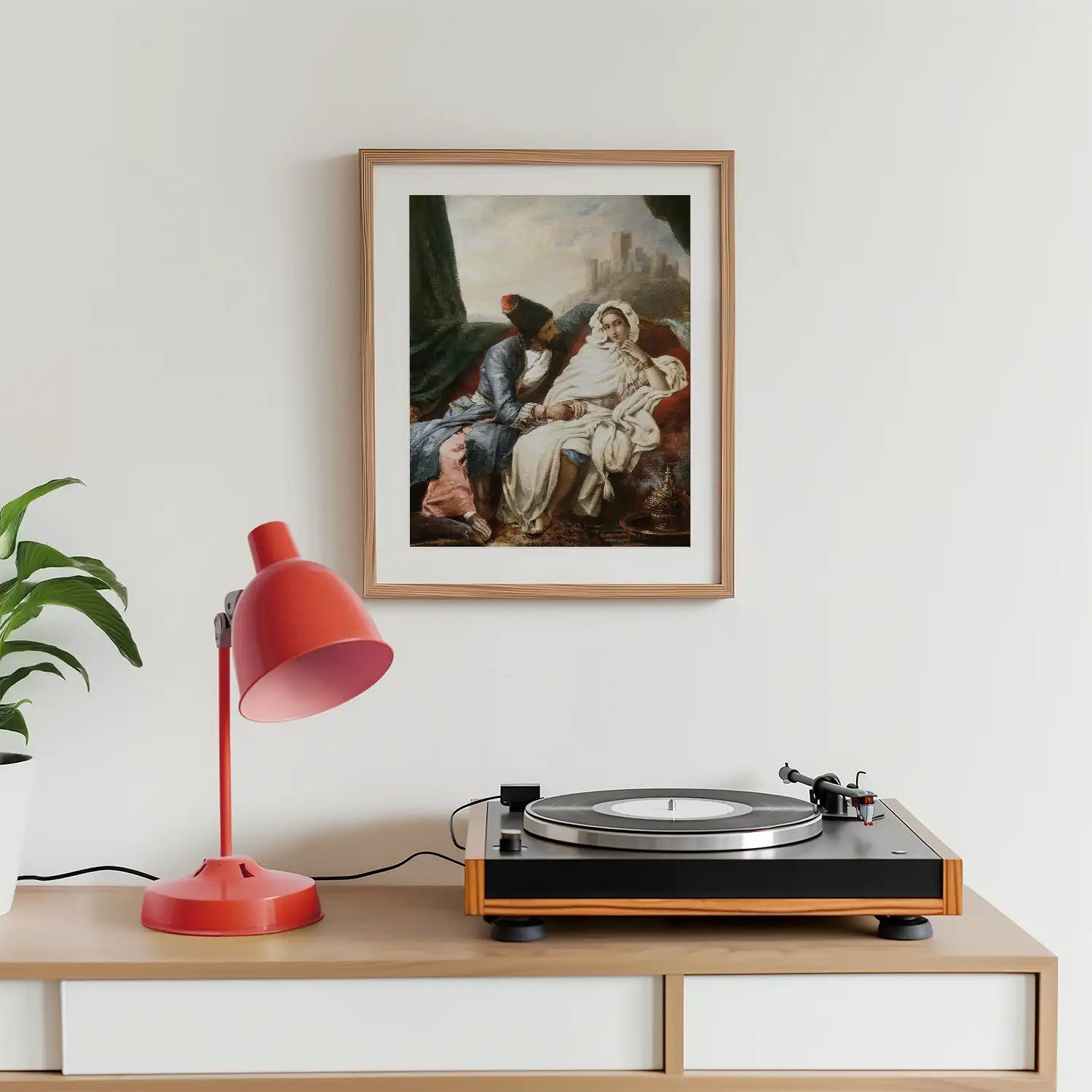 Framed painting of two figures in a serene landscape, displayed above a record player and a pink lamp on a wooden surface.