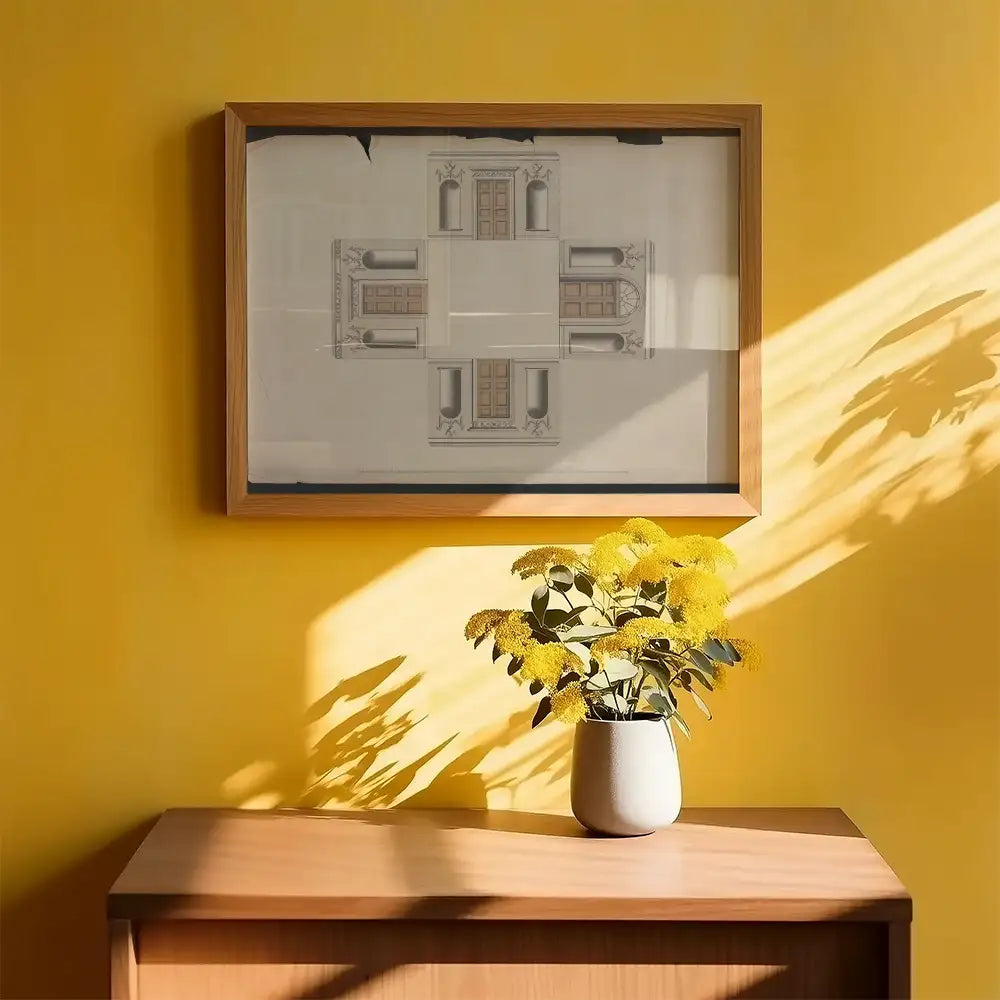 Framed architectural print hanging on a yellow wall above a wooden side table with a vase of yellow flowers.