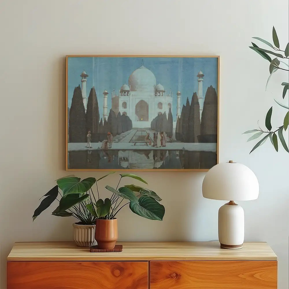 Framed painting of the Taj Mahal with people walking beside a reflecting pool, displayed on a light-colored wall above a wooden sideboard with a potted plant and a modern lamp.