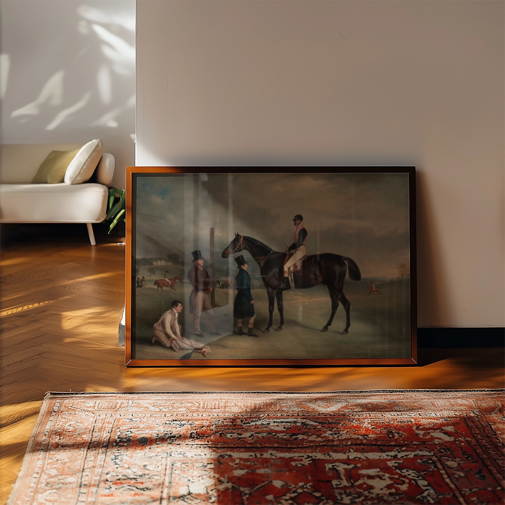 Framed painting of a horse with riders and spectators in a pastoral setting, displayed on a wooden floor next to a carpet and a modern chair.