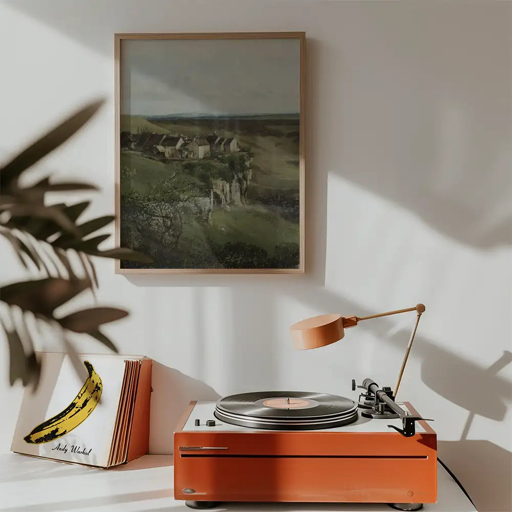 Painting of a rural landscape with a farmhouse, framed on a wall above a record player and a stack of albums, featuring a banana artwork.