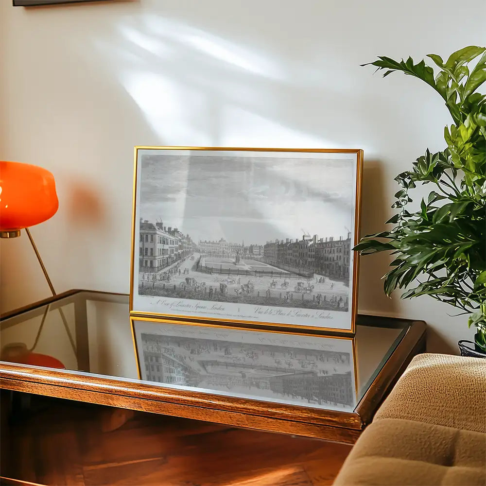 Framed black and white print depicting a historical view of London, placed on a wooden table with a decorative lamp and plant nearby.