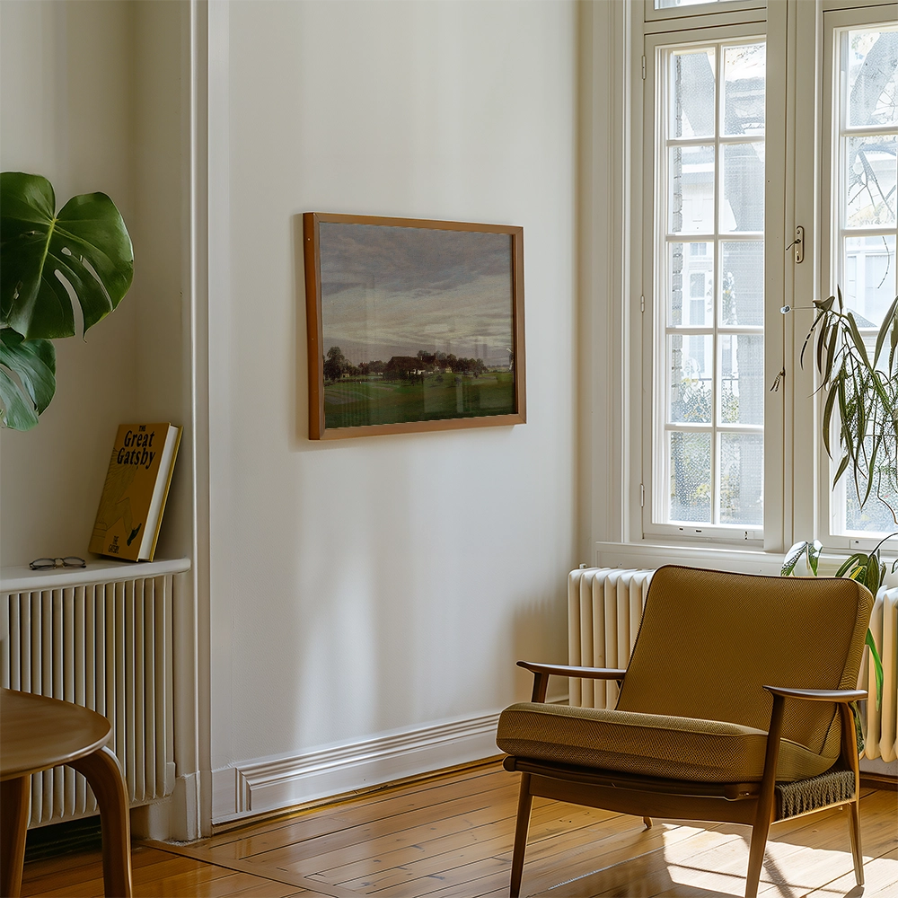 Framed painting of a landscape hanging on a wall in a cozy living room with a brown armchair and a nearby potted plant.