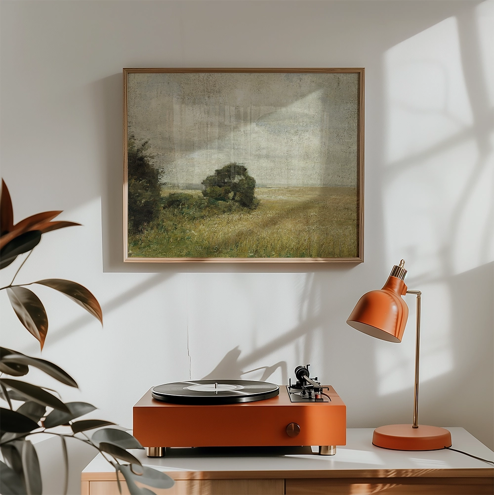 Framed painting of a serene landscape with a tree and golden fields, displayed on a wall above an orange record player and lamp in a stylish interior setting.