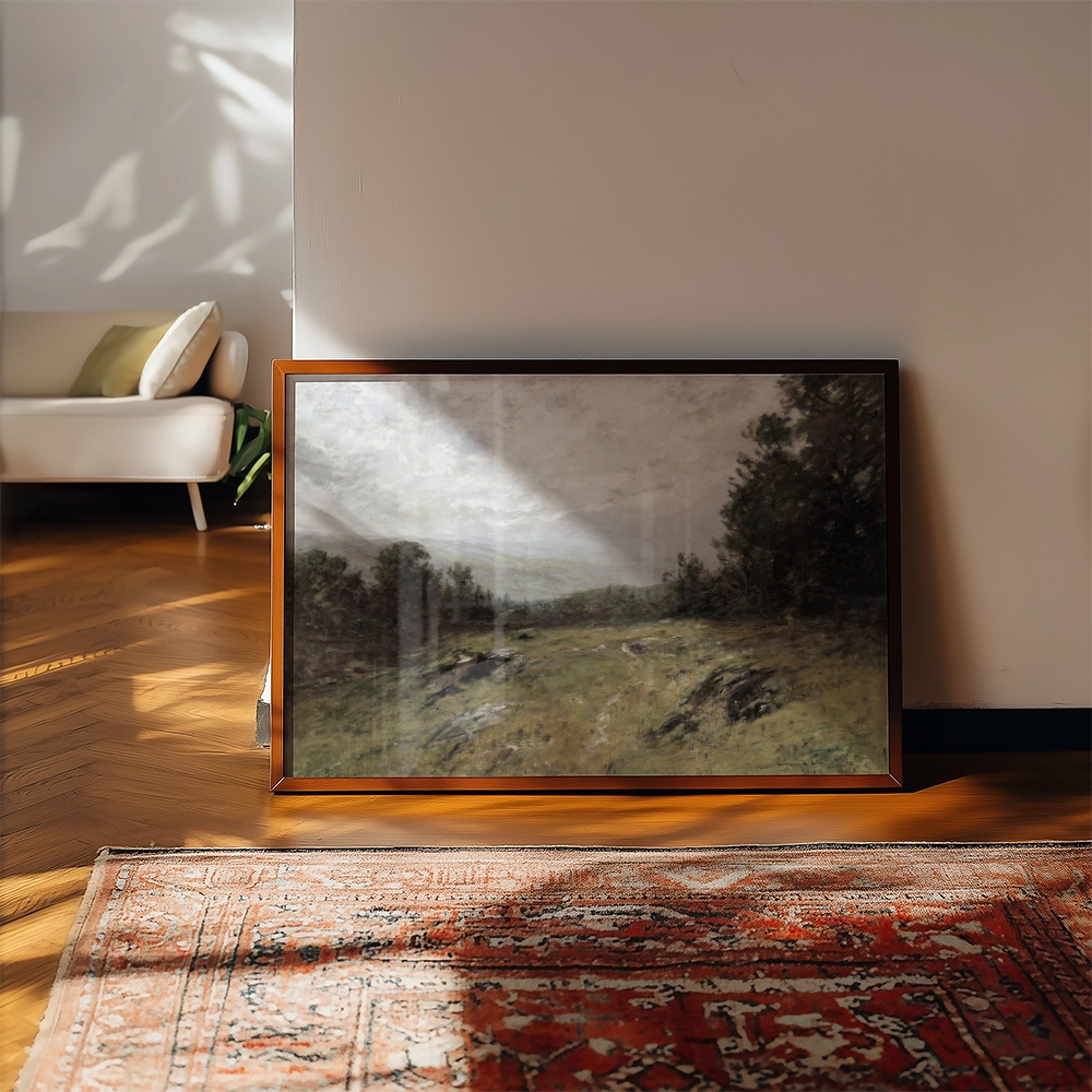 Framed landscape painting resting against a wall in a sunlit room with a patterned rug and a sofa in the background.