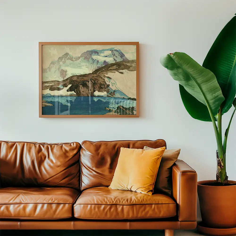Framed landscape painting of mountains and a lake above a leather sofa with a yellow cushion and a potted plant.