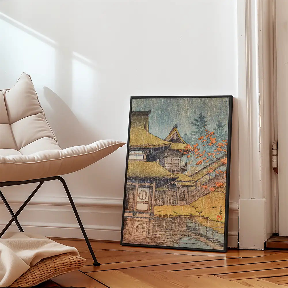 Framed painting of a traditional Japanese landscape with a house and autumn foliage, placed next to a modern chair in a bright room.
