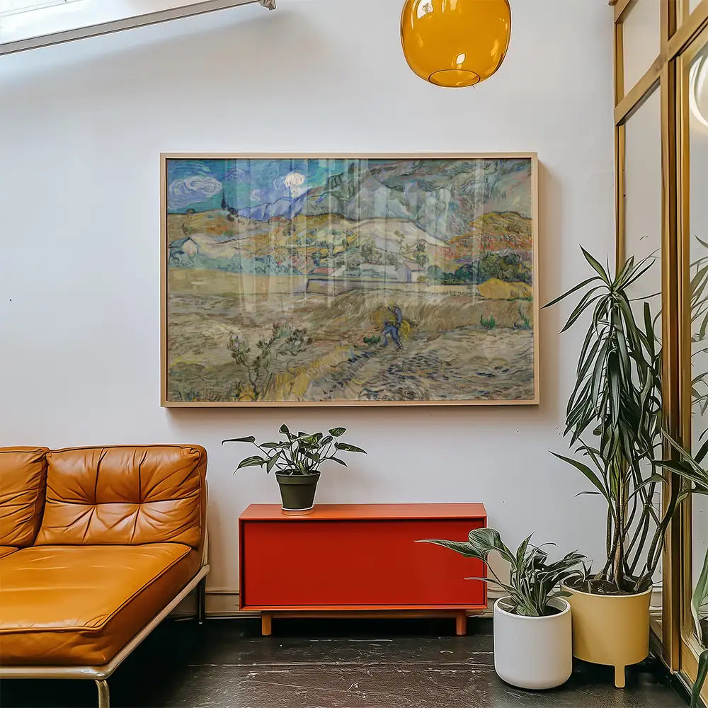 Framed painting of a landscape hanging above a modern orange sofa in a stylish interior setting with plants and a red cabinet.